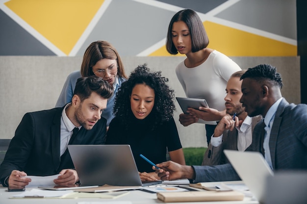 Un equipo de jóvenes empresarios confiados mirando una computadora portátil mientras se reúnen juntos en la oficina