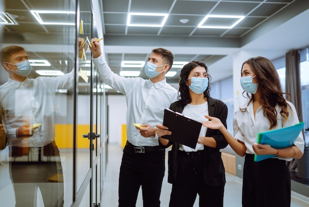 Foto equipo de jóvenes empresarios en mascarilla protectora en proyecto corporativo juntos.