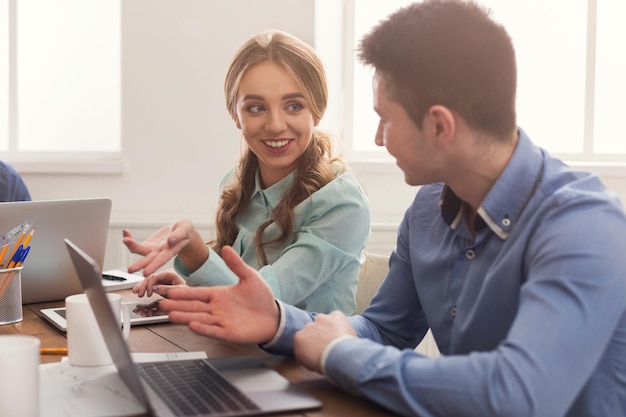 Equipo de jóvenes programadores que trabajan en una empresa de desarrollo de software, escribiendo en computadoras portátiles, hombre y mujer sonriendo el uno al otro y discutiendo el proyecto, espacio de copia