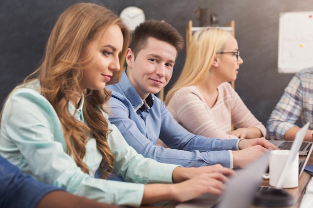 Equipo de jóvenes programadores que trabajan en una empresa de desarrollo de software, escribiendo en computadoras portátiles, probando nuevos juegos o aplicaciones, copia espacio