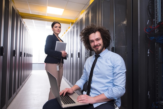 Equipo de jóvenes técnicos que trabajan juntos en servidores en el centro de datos utilizando computadoras portátiles y tabletas