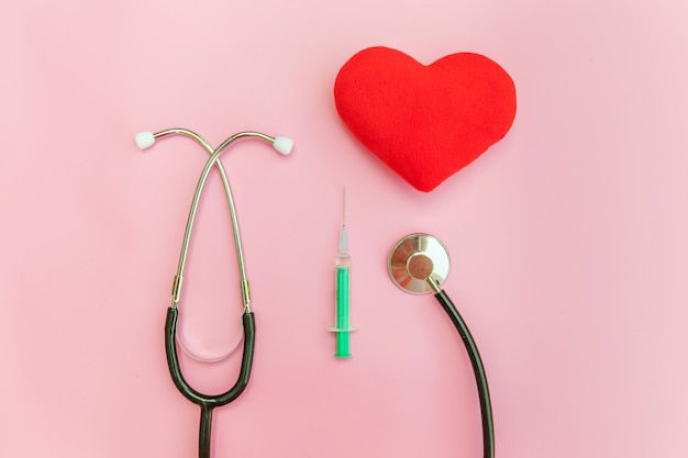 Equipo de medicina estetoscopio o fonendoscopio jeringa y corazón rojo aislado sobre fondo rosa pastel de moda