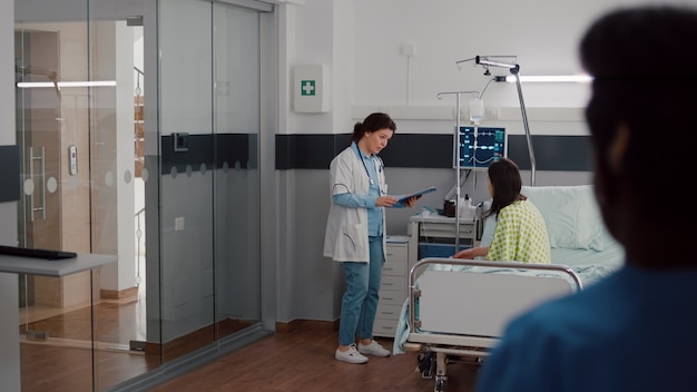 Equipo médico que controla la frecuencia cardíaca de monitoreo vital del paciente ayudando con la bolsa de goteo de líquidos