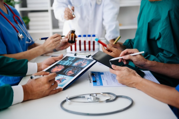 Equipo médico reunido con médicos con batas blancas de laboratorio y uniformes quirúrgicos sentados en una mesa discutiendo sobre pacientes que trabajan en línea usando computadoras en la industria médica