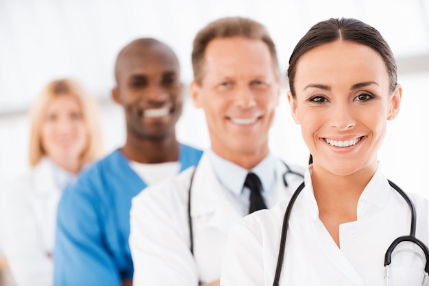 Foto equipo de médicos confiados. doctora confiada mirando a cámara y sonriendo mientras sus colegas de pie en una fila detrás de ella