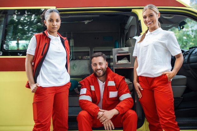 Un equipo de médicos felices y sonrientes trabajando junto a la ambulancia.