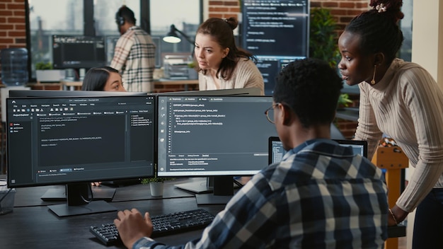 Equipo mixto de programadores en la nube de inteligencia artificial hablando de programación frente a múltiples pantallas compilando código. Programadores haciendo trabajo en equipo mirando algoritmos de aprendizaje automático.