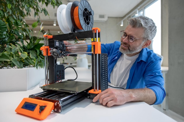 Equipo moderno de impresora 3D y hombre que trabaja con él en la oficina