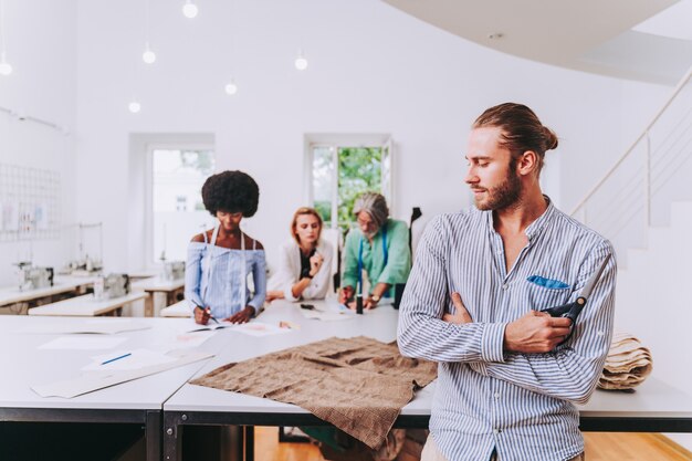 Equipo multiétnico de diseñadores de moda que trabajan en un taller de puesta en marcha de ropa: grupo multirracial de estilistas, sastres y modistas que trabajan en una nueva colección.