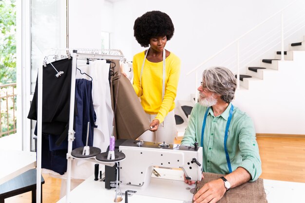 Equipo multiétnico de diseñadores de moda que trabajan en un taller de puesta en marcha de ropa: grupo multirracial de estilistas, sastres y modistas que trabajan en una nueva colección.