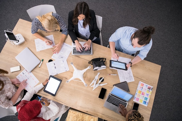 equipo multiétnico de empresas emergentes discutiendo un nuevo plan de negocios, trabajando en computadoras portátiles y tabletas mientras aprende sobre la tecnología de drones para futuras empresas comerciales vista superior