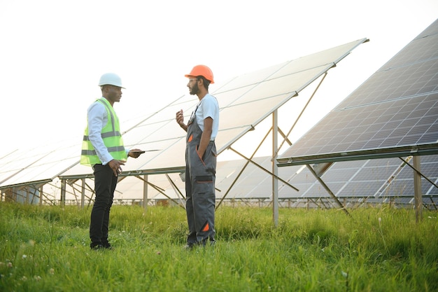 Equipo multirracial de ingenieros en paneles solares Ingeniero afroamericano y árabe trabajando en una granja de paneles solares