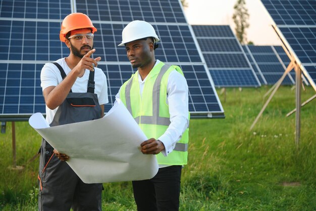 Equipo multirracial de ingenieros en paneles solares ingeniero afroamericano y árabe trabajando en una granja de paneles solares