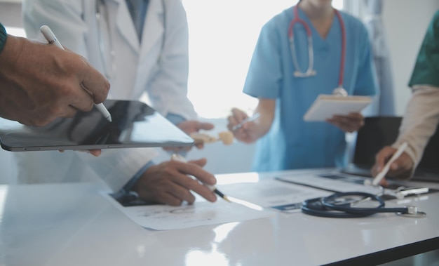 Equipo multirracial de médicos discutiendo sobre un paciente de pie agrupado en el vestíbulo mirando una vista de cerca de una tableta