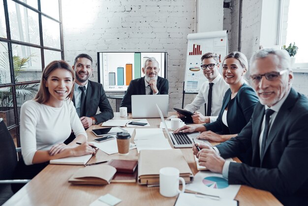 Equipo de negocios exitoso sonriendo y mirando a la cámara mientras trabaja en la oficina moderna