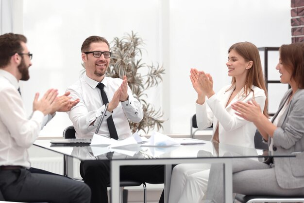 Equipo de negocios feliz aplaudiendo mientras está sentado en su escritorio el concepto de una puesta en marcha exitosa