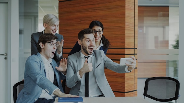 Equipo de negocios feliz tomando un retrato selfie en la cámara del teléfono inteligente y posando para una foto grupal