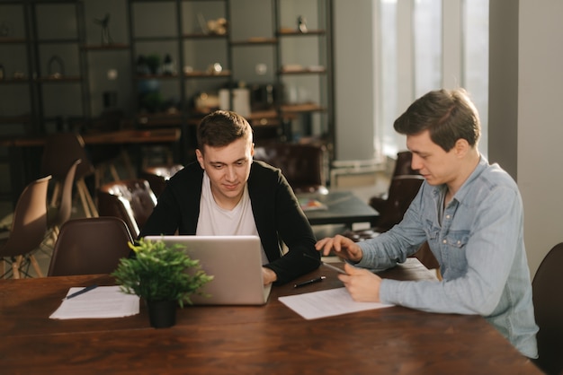 Equipo de negocios hombres jóvenes hablando de estrategia con portátil en la oficina moderna