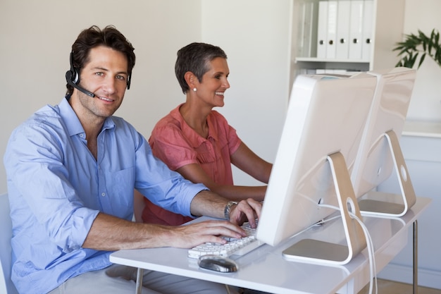 Foto equipo de negocios informal trabajando en escritorio usando computadoras con hombre sonriendo a la cámara