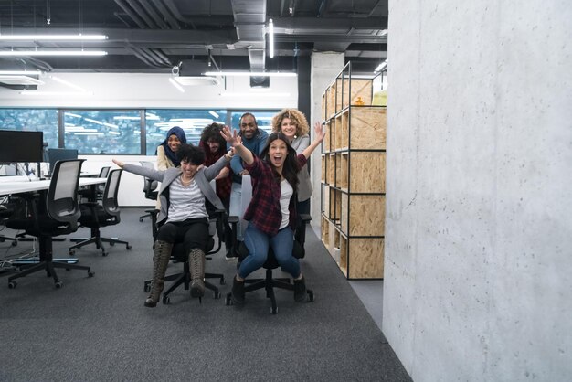 Equipo de negocios de inicio multiétnico de desarrolladores de software que se divierten mientras compiten en sillas de oficina, empleados diversos emocionados riendo disfrutando de una actividad divertida en el descanso del trabajo, trabajadores creativos y amigables p