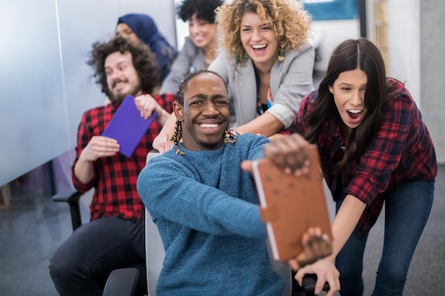 Equipo de negocios de inicio multiétnico de desarrolladores de software que se divierten mientras compiten en sillas de oficina, empleados diversos emocionados riendo disfrutando de una actividad divertida en el descanso del trabajo, trabajadores creativos y amigables p