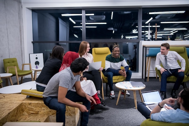 Equipo de negocios de inicio multiétnico en reunión en una moderna y brillante lluvia de ideas en el interior de la oficina, trabajando en una computadora portátil y una tableta