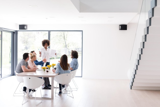 Equipo de negocios de inicio multiétnico en reunión en una moderna y brillante lluvia de ideas en el interior de la oficina, trabajando en una computadora portátil y una tableta