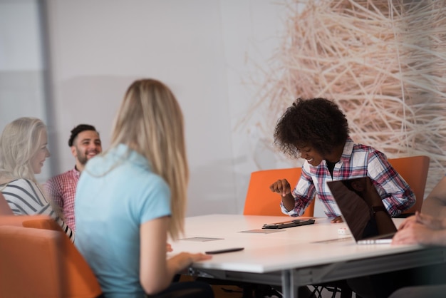 Equipo de negocios de inicio multiétnico en reunión en una moderna y brillante lluvia de ideas en el interior de la oficina, trabajando en una computadora portátil y una tableta