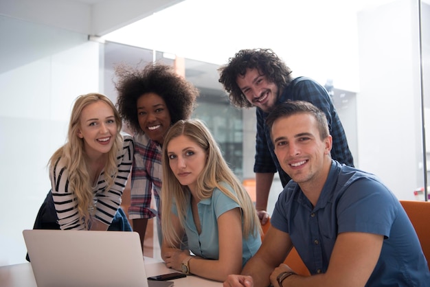 Equipo de negocios de inicio multiétnico en reunión en una moderna y brillante lluvia de ideas en el interior de la oficina, trabajando en una computadora portátil y una tableta