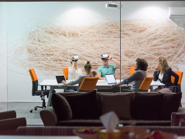 Equipo de negocios de inicio que utiliza auriculares de realidad virtual en una reunión nocturna de la oficina Reunión de desarrolladores con un simulador de realidad virtual alrededor de una mesa en una oficina creativa.