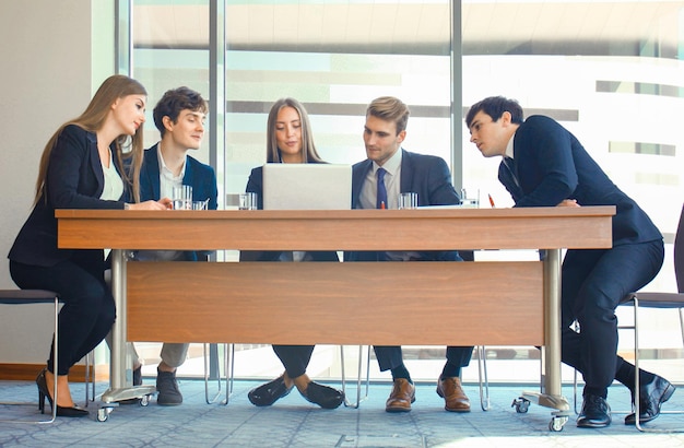 Equipo de negocios de inicio en la reunión en el interior de la oficina moderna y luminosa lluvia de ideas trabajando en una computadora portátil y una tableta