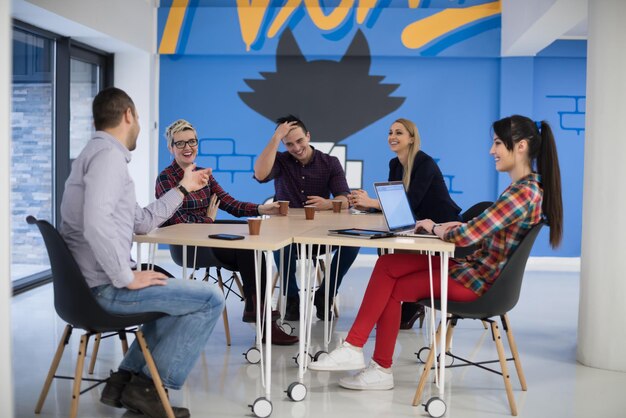 Equipo de negocios de inicio en reunión en la lluvia de ideas interior de la oficina moderna y luminosa, trabajando en una computadora portátil y tableta