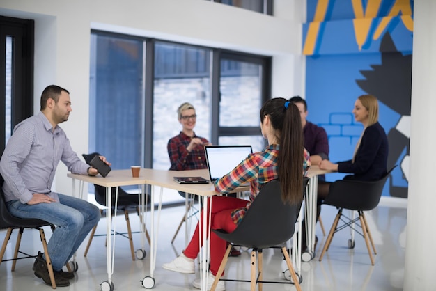 Equipo de negocios de inicio en reunión en la lluvia de ideas interior de la oficina moderna y luminosa, trabajando en una computadora portátil y tableta