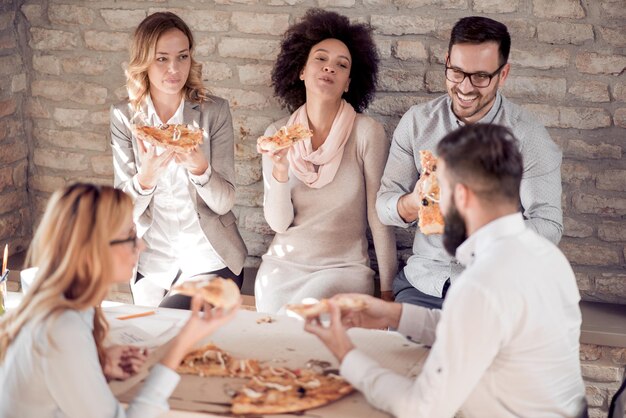 Equipo de negocios joven feliz comiendo pizza en la oficina