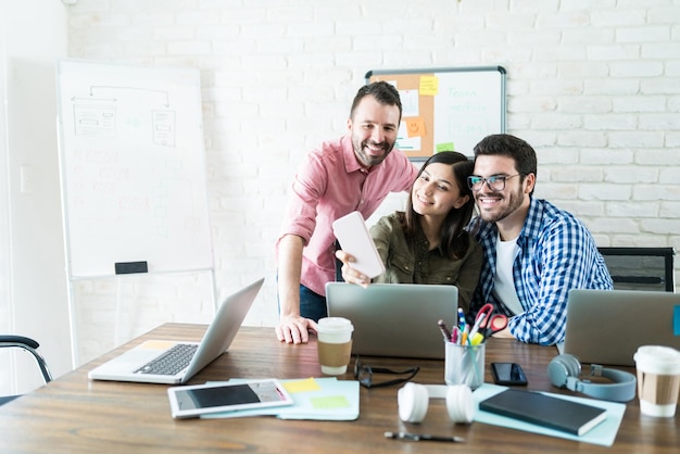 Equipo de negocios latino tomando autorretrato en teléfono móvil en la sala de reuniones en la oficina