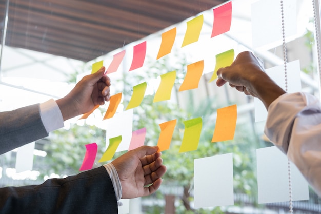 Equipo de negocios mira las notas adhesivas en la pared de vidrio en la sala de reuniones