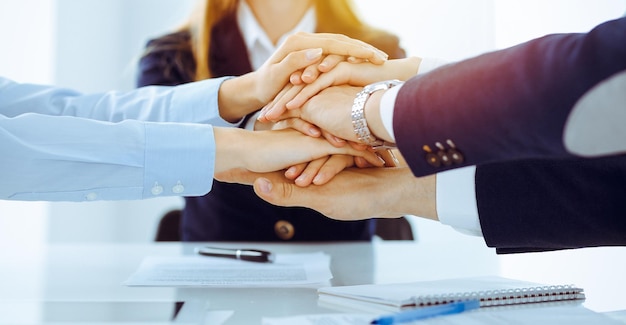 Equipo de negocios mostrando unidad con las manos juntas en una oficina soleada. Grupo de personas uniéndose y representando el concepto de amistad y trabajo en equipo