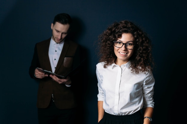 Equipo de negocios mujer rizada con líder de gafas y asistente masculino joven sobre un fondo oscuro