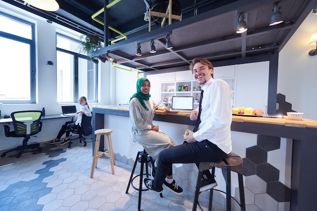 equipo de negocios multicultural internacional. hombre comiendo manzana mujer musulmana africana usando hiyab verde bebiendo té mientras trabajan juntos en una computadora portátil en el área de relajación en el moderno plan abierto startu