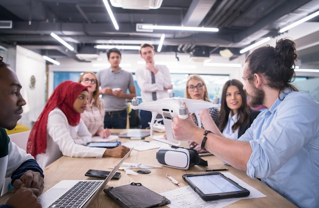 equipo de negocios multiétnico de inicio discutiendo un nuevo plan de negocios, trabajando en una computadora portátil y una tableta mientras aprende sobre la tecnología de drones para el avance de nuevos negocios
