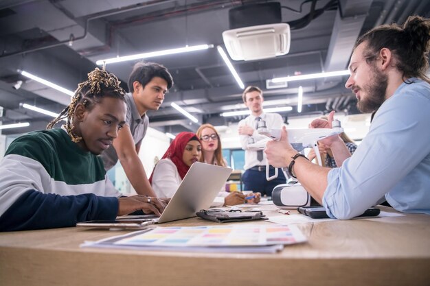 equipo de negocios multiétnico de inicio discutiendo un nuevo plan de negocios, trabajando en una computadora portátil y una tableta mientras aprende sobre la tecnología de drones para el avance de nuevos negocios