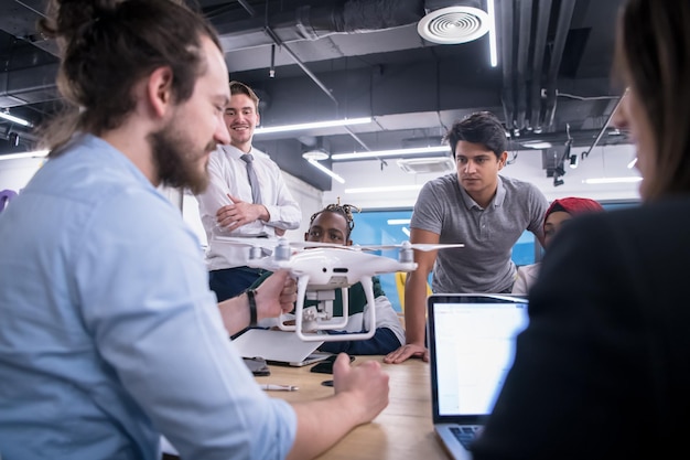 equipo de negocios multiétnico de inicio discutiendo un nuevo plan de negocios, trabajando en una computadora portátil y una tableta mientras aprende sobre la tecnología de drones para el avance de nuevos negocios