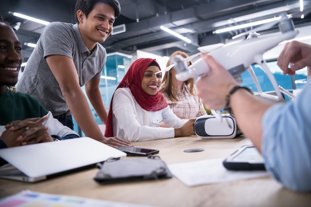 equipo de negocios multiétnico de inicio discutiendo un nuevo plan de negocios, trabajando en una computadora portátil y una tableta mientras aprende sobre la tecnología de drones para el avance de nuevos negocios