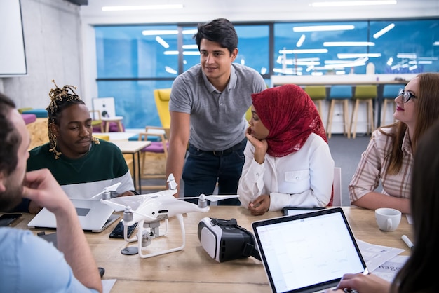 equipo de negocios multiétnico de inicio discutiendo un nuevo plan de negocios, trabajando en una computadora portátil y una tableta mientras aprende sobre la tecnología de drones para el avance de nuevos negocios