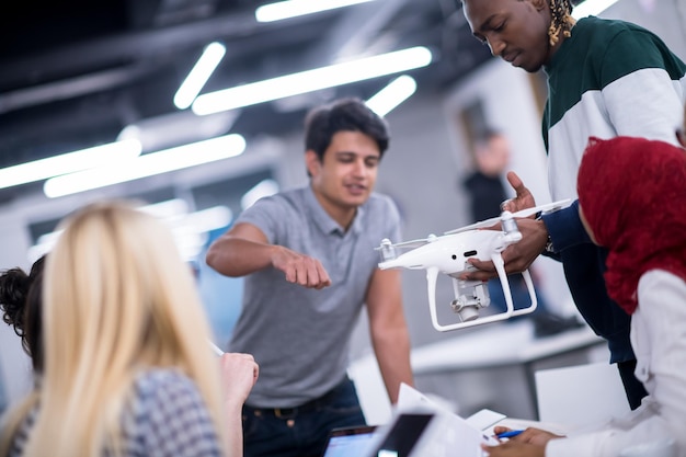 equipo de negocios multiétnico de inicio discutiendo un nuevo plan de negocios, trabajando en una computadora portátil y una tableta mientras aprende sobre la tecnología de drones para el avance de nuevos negocios