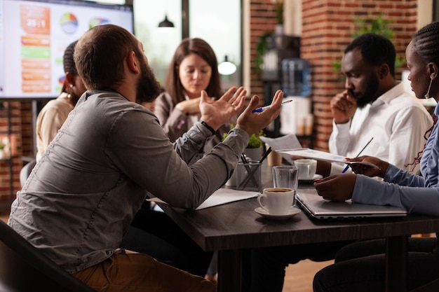 Equipo de negocios multiétnico que desarrolla un proyecto de marketing que discute la estrategia de la empresa durante una reunión de negocios en la oficina de inicio. Empresarios analizando gráfico financiero, lluvia de ideas