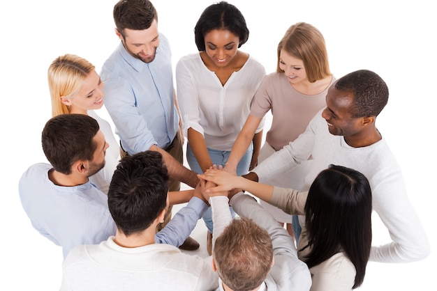 Equipo orgullosamente exitoso. Vista superior del grupo diverso positivo de personas en ropa casual elegante manteniendo sus manos juntas y sonriendo mientras están de pie cerca uno del otro