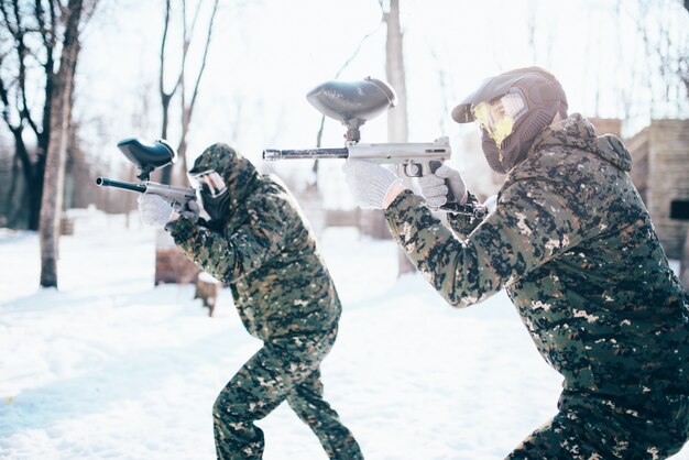 Equipo de paintball en ataque uniforme en batalla de invierno. Juego de deporte extremo, soldados con máscaras de protección y camuflaje con arma en las manos.