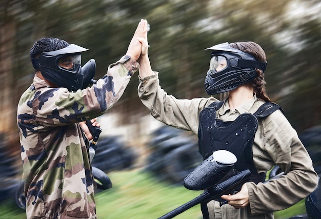 Equipo de paintball y choca los cinco por ganar el logro de la victoria o tiempo de juego exitoso en el campo Hombre y mujer celebrando juntos la victoria en la guerra en deportes extremos y tocándose las manos en el trabajo en equipo