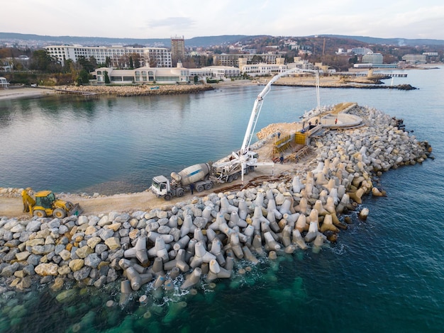 El equipo pesado de construcción está construyendo un rompeolas Vertiendo hormigón en un muelle en construcción en el mar